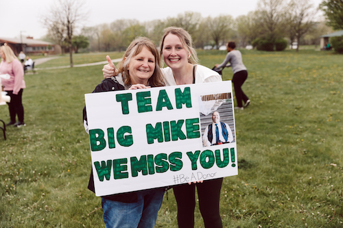 Woman holding a handmade sign that reads 'Team Big Mike. We Miss You'